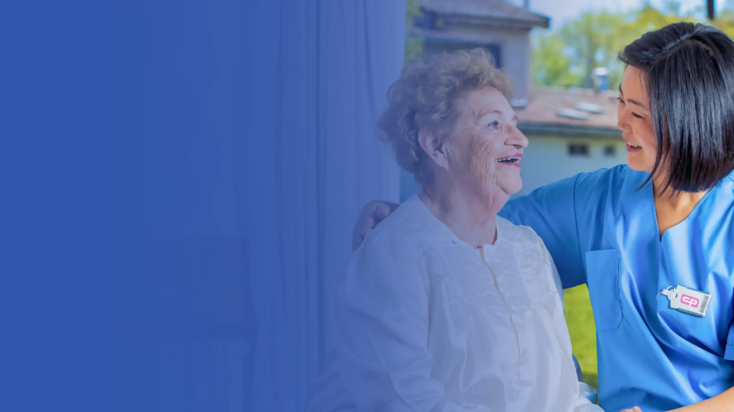 Caregiver smiling with an elderly woman, providing supportive home care and companionship.